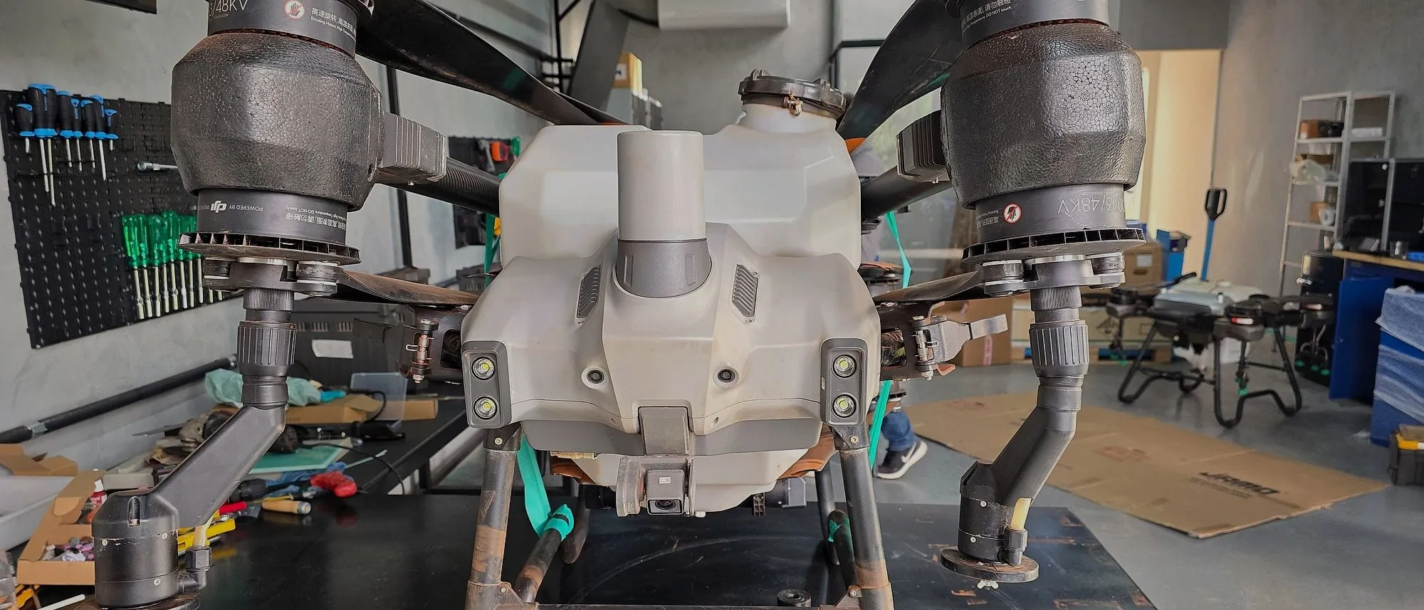 Drone DJI Agras visto de frente na bancada do laboratório de assistência técnica